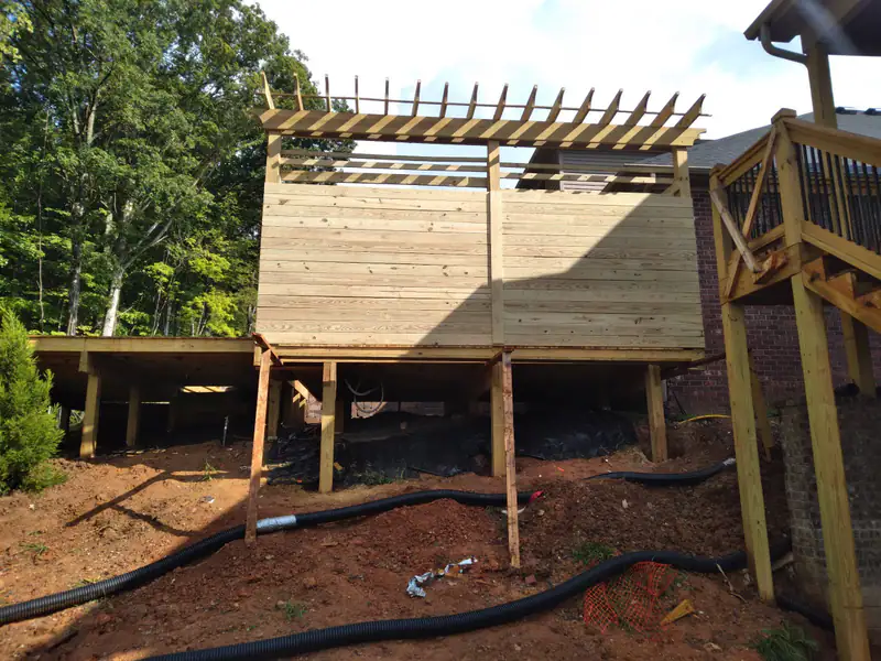Pergola deck going up on posts over a sloped yard, with drainage pipe laid underneath