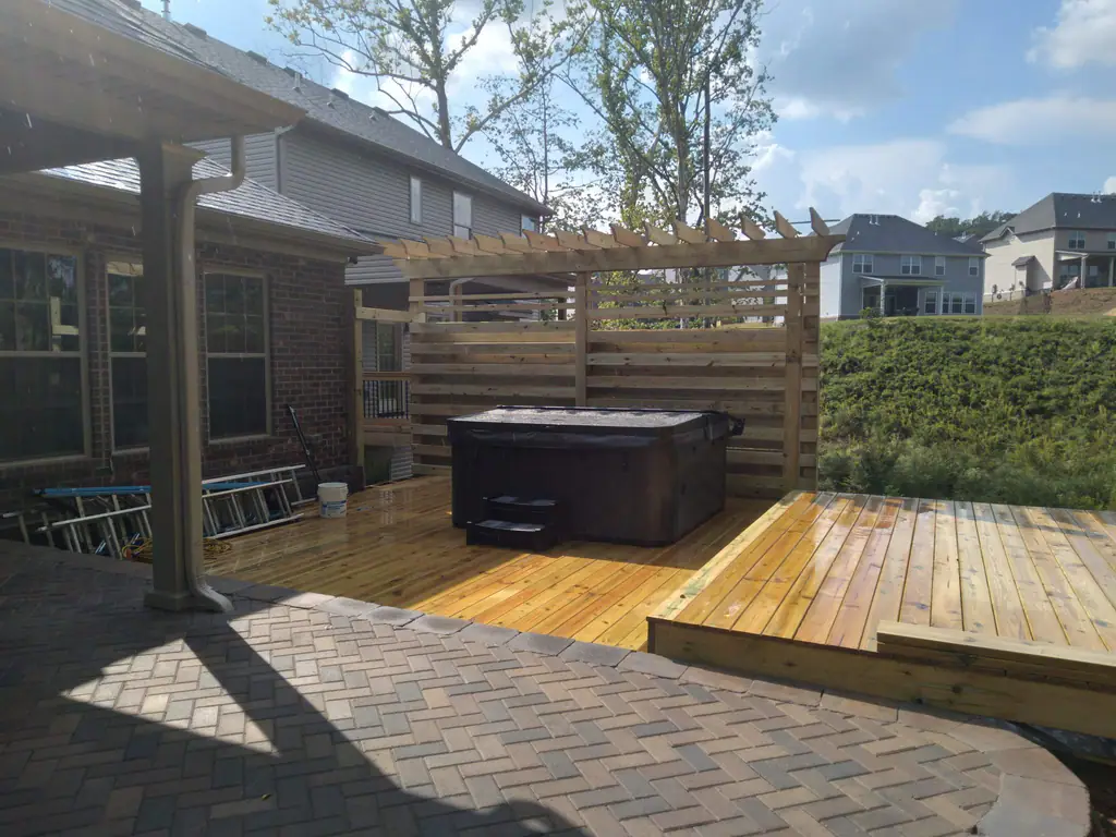 New pergola deck with a slatted privacy screen around a hot tub, beside a herringbone paver patio