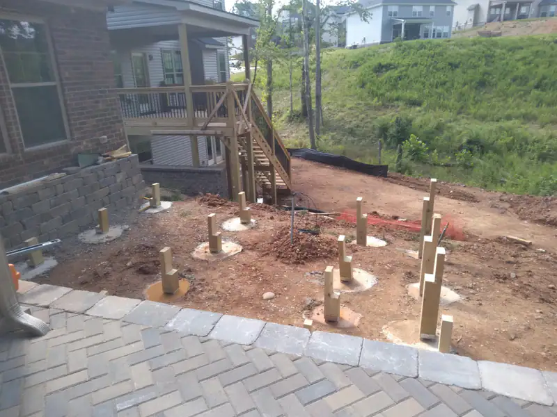 Deck posts set in the ground beside a paver patio, the start of a pergola deck
