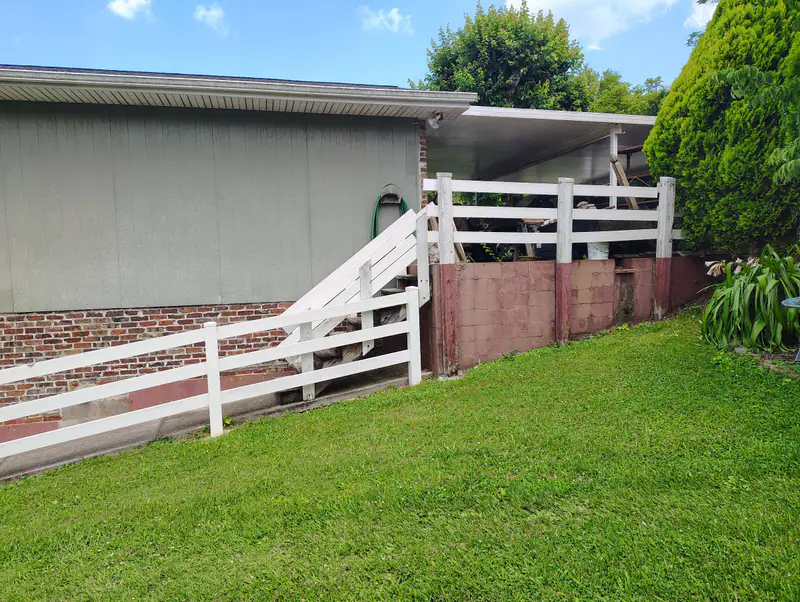 New back stairs and white rail fence along a sloped lawn