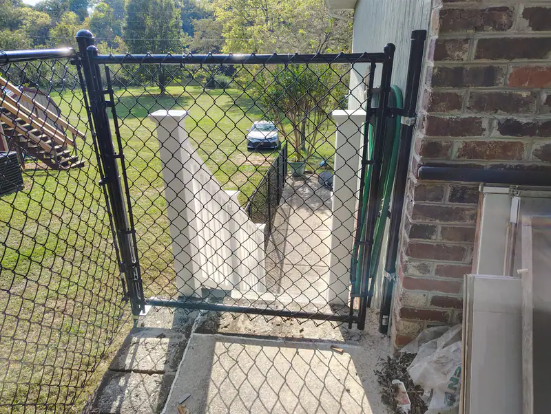 Chain-link walk gate between a brick house and the fence line