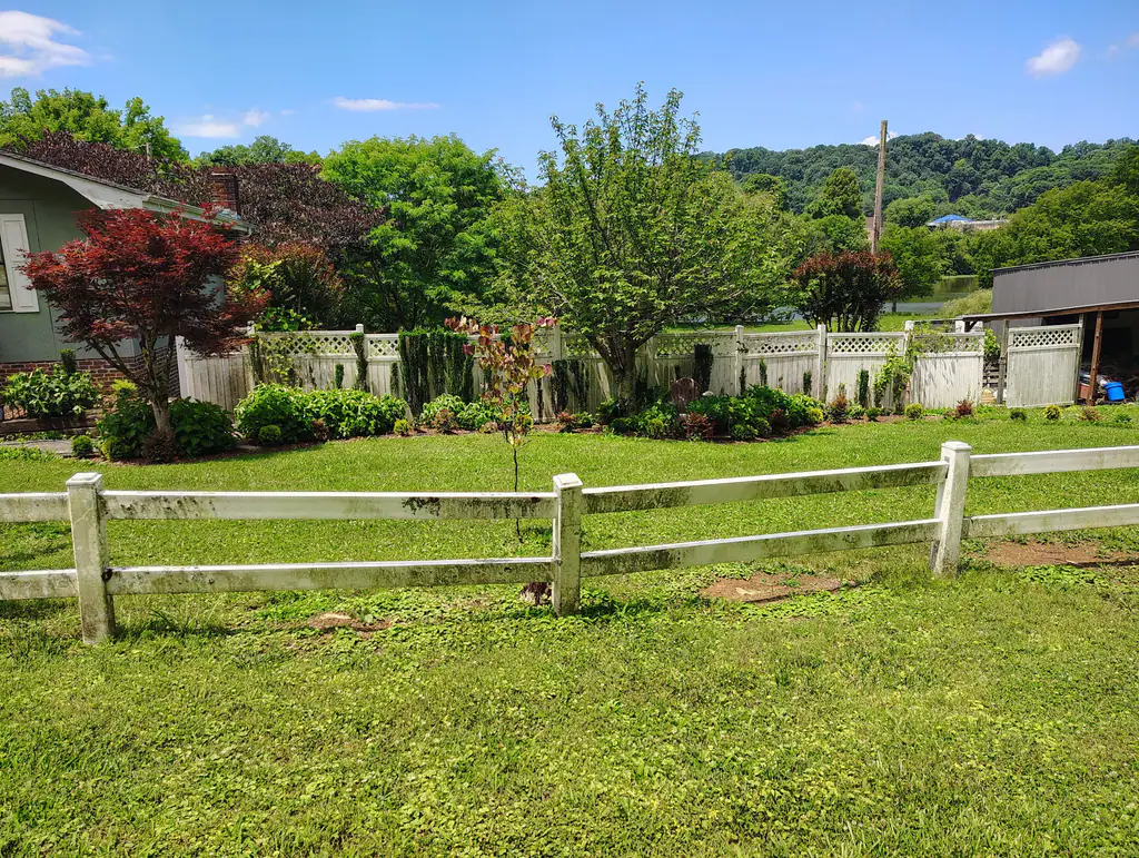 White two-rail fence across a green yard with East Tennessee hills behind