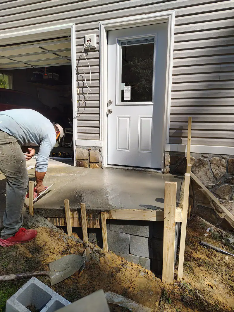 Crew finishing a fresh concrete pad at a side door