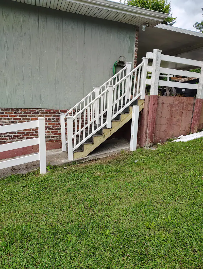 Rebuilt back stairs with white vinyl railings beside a new two-rail fence