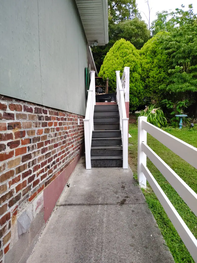 Concrete walk and new steps with white railings along a brick house